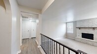 Located at 5109 N Brookline Ave in Oklahoma City, this single-story unit presents a thoughtfully designed layout with a clean, neutral aesthetic throughout. The floor plan, visible in the 3D model, reveals a well-organized interior with distinct living, kitchen, bedroom, and hallway areas connected by arched doorways that add a subtle architectural detail.

The living area is a standout space, anchored by a striking stone fireplace with a wood mantel and framed by a window fitted with blinds that allow natural light to filter in. Soft carpet flooring enhances the comfort of this area. A dark-railed staircase balustrade along the upper landing adds visual contrast against the light walls.

The kitchen features gray shaker-style cabinetry, white subway tile backsplash, light quartz-look countertops, and wood-look vinyl flooring. It is equipped with a gas range, dishwasher, and stainless steel refrigerator, offering a functional and updated cooking space.

Bedrooms are carpeted and well-sized, with at least one featuring a walk-in closet with shelving. Ceiling fans provide additional comfort, and windows bring in natural light. The bathroom includes a tub-shower combination, a vanity with marble-look countertops, and wood-look vinyl flooring, maintaining the cohesive, updated style found throughout the unit.
