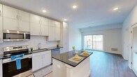 Located at 37 North York Road in Hatboro, PA, this thoughtfully designed one-bedroom, two-bathroom residence offers a clean, modern aesthetic throughout its efficiently laid-out single floor. The open-concept living and kitchen area serves as the heart of the home, showcasing light hardwood flooring, recessed lighting, and a bright, airy atmosphere. The kitchen is well-appointed with white shaker-style cabinetry extending to the ceiling for ample storage, dark granite countertops, a classic subway tile backsplash, and a full suite of stainless steel appliances including a range, microwave, dishwasher, and refrigerator. A central island with matching granite provides additional prep and dining space. The spacious bedroom features two windows that allow natural light to fill the room, offering views of the surrounding greenery. A barn-style sliding door adds a modern touch and leads to a dedicated closet. Both bathrooms are finished with neutral tile flooring, white vanities with granite countertops, and clean white walls, maintaining the home's cohesive, contemporary style. A private balcony overlooks a well-maintained parking area with landscaped surroundings. The unit includes convenient on-site parking.