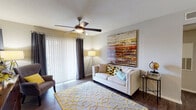 This single-floor residence offers a thoughtfully designed layout that balances comfort and functionality across its key living spaces. The living room serves as the heart of the home, featuring rich hardwood-style flooring, a ceiling fan with integrated lighting, and a large sliding glass door dressed with vertical blinds and dramatic charcoal drape panels that invite an abundance of natural light. The space flows seamlessly into a dedicated dining area, which is defined by a pendant light fixture overhead and provides an intimate setting for meals.

The galley-style kitchen is efficiently arranged with white cabinetry, granite-look countertops, a subway tile backsplash, and a full suite of stainless steel appliances, including a refrigerator, electric range, microwave, and dishwasher. Light wood-tone flooring ties the kitchen visually to the rest of the home.

The bedroom is a calm retreat, equipped with its own ceiling fan, direct outdoor access through a secondary door, and ample wall space. Neutral tones and warm lighting create a restful atmosphere throughout.

The bathroom features a clean, white-tiled soaking tub and shower combination alongside a vanity with granite-look countertops and hardwood-style flooring, maintaining the cohesive aesthetic found throughout the residence.
