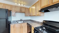 This two-floor residence is designed with practical functionality and comfortable living in mind. The kitchen is well-appointed, featuring light natural wood cabinetry with sleek bar-pull hardware that extends both above and below the dark laminate countertops. A stainless steel sink is positioned along the counter, complemented by a black gas range and a dishwasher, providing a full suite of appliances for everyday use. Track lighting overhead illuminates the workspace effectively, while ample cabinet storage ensures organizational convenience throughout.

The main living level showcases hardwood-style flooring that extends from the kitchen area through to the living space, creating a cohesive and easy-to-maintain surface. A set of French doors at the far end of the living area brings in natural light and adds an elegant architectural touch to the space.

A carpeted staircase connects the two floors, offering a soft, comfortable transition to the upper level. The neutral color palette throughout—white walls paired with warm wood tones and dark appliances—creates a balanced, inviting ambiance that suits a variety of furnishing styles. The overall layout emphasizes open sightlines and accessibility between key living areas.