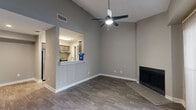 This two-story, two-bedroom, two-bathroom residence is thoughtfully laid out across two floors, with the majority of the living space on the main level and a private bedroom suite above. The main floor features an open-concept living, dining, and kitchen area with vaulted ceilings, a ceiling fan, and wood-look flooring throughout. A built-in fireplace with a tile hearth anchors the living area, while large sliding glass doors fitted with vertical blinds fill the space with natural light and provide access to a private patio. The kitchen connects to the living area through a pass-through window with a breakfast bar, and is equipped with cabinetry and standard appliances including a refrigerator. A staircase leads to the upper level, where the primary bedroom offers plush carpeting, a ceiling fan, a window with natural views, and direct access to a dedicated closet. The primary bathroom features a vanity with a stone-topped surface, dark wood cabinetry, and a large mirror. A second bedroom on the main level also offers carpeting, a ceiling fan, and a walk-in closet. The second bathroom includes a full tub-shower combination with large-format tile surround and chrome fixtures. A laundry area and additional closet storage complete this well-appointed, functional home.