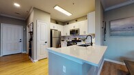 This single-floor residence is thoughtfully designed with a cohesive neutral palette and modern finishes throughout. The kitchen serves as a functional centerpiece, outfitted with white shaker cabinetry, a marble-style tile backsplash, stainless steel appliances including a gas range and built-in microwave, and light quartz countertops extending to a peninsula with seating. Light hardwood-style flooring runs through the kitchen and living areas, adding warmth to the space.

The living room is anchored by a striking fireplace with a black tile surround and white mantel, complemented by crown molding and neutral gray walls that create a calm, inviting atmosphere. The space connects naturally to the rest of the home.

Two bedrooms provide comfortable retreats, each with plush carpet, neutral tones, and ample room. One bedroom features large windows allowing natural light to fill the space. The bathrooms are finished with white cabinetry, black hardware accents, and classic white tile with black border detailing, including a soaking tub and a separate tub-shower combination. A dedicated in-unit laundry area with a full-size washer and dryer, wire shelving, and hardwood-style flooring rounds out the practical features of this well-designed home.