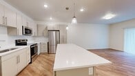 Located at 12338 S Pony Express Rd in Draper, Utah, this well-appointed 1-bedroom, 1-bathroom unit offers a thoughtfully designed single-floor layout. The open-concept kitchen and living area serves as the heart of the space, showcasing warm luxury vinyl plank flooring, crisp white walls, and an abundance of natural light. The kitchen is outfitted with sleek, light-toned cabinetry, white quartz countertops, a full suite of stainless steel appliances—including a refrigerator, range, microwave, and dishwasher—and a spacious center island illuminated by elegant pendant lighting, ideal for both meal prep and casual dining. The adjoining living area is bright and open, featuring a sliding glass door with vertical blinds that allows natural light to pour in and provides access to the outdoors. The bedroom offers a comfortable, carpet-floored retreat with a window dressed with blinds. The bathroom is clean and modern, featuring a tub-shower combination, a vanity with a white countertop, and a large mirror. A dedicated laundry area with a full-size stacked washer and dryer adds everyday convenience. The overall ambiance is fresh, modern, and move-in ready.