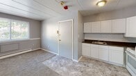 Located at 1300 Renshaw Rd in Chester, PA, this single-floor unit offers a straightforward, functional layout well-suited for everyday living. The open-concept area seamlessly connects the kitchen and living space, with a clear transition between tile-style flooring in the kitchen and soft carpeting in the living and bedroom areas. The kitchen is well-appointed with white shaker-style cabinetry, dark granite-look countertops, a classic white subway tile backsplash, a gas range, and a full-size refrigerator — providing ample storage and workspace. A stainless undermount sink adds a practical touch. The living area is finished in a neutral gray two-tone paint scheme with white trim, creating a clean and calm atmosphere. Baseboard heating units are present throughout, ensuring warmth during cooler months. The carpeted rooms are generously proportioned, with windows that allow natural light to filter in. One room includes a double-door closet, offering useful storage. The full bathroom features a white vanity, a tub-shower combo, blue accent tile detailing, and a patterned floor — providing a tidy and functional space. The unit's paneled ceilings and consistent neutral palette throughout give it a cohesive, move-in-ready appearance.