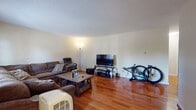 This single-floor residence in Manchester, CT offers a well-organized layout with consistent hardwood flooring throughout the main living spaces. The living room is generously sized, accommodating a large sectional sofa and media setup, and features multiple windows that allow natural light to filter in, offering views of the surrounding neighborhood. A textured ceiling adds subtle character to the room.

The kitchen has been thoughtfully updated with cream-toned raised-panel cabinetry extending to the upper walls, providing ample storage. A mosaic tile backsplash in blue and gray tones adds visual interest, complementing the granite-style countertops. Stainless steel appliances — including a refrigerator, range, over-the-range microwave, and dishwasher — complete the functional cooking space. Light wood-look flooring runs throughout the kitchen area.

The bedroom is a comfortable, well-proportioned room featuring the same warm hardwood flooring, a sliding-door closet, and a window with blinds providing privacy and natural light. The bathroom includes tile flooring, a modern vanity with a white basin, a mirrored medicine cabinet, a tile backsplash, and a shower-tub combination. Overall, the space presents a practical and updated interior suitable for comfortable everyday living.