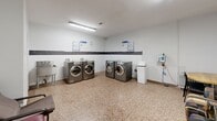 Located at 4141 Bathurst Street in Toronto, Ontario, this shared laundry facility offers a practical and well-organized space for residents. The room is finished with durable terrazzo flooring throughout, white painted walls accented by a horizontal band of dark grey tile, and bright fluorescent overhead lighting that ensures excellent visibility.

The laundry area is equipped with multiple front-loading LG washers and dryers arranged along the walls, providing ample capacity for residents. Instructional signage for washer and dryer usage is clearly posted above the machines, and a wall-mounted clock keeps track of cycle times. A utility sink is available along one wall, and a payment station is conveniently positioned nearby.

A waiting area adjacent to the laundry machines offers comfortable seating, including armchairs and a small table, making it easy for residents to wait during their laundry cycles. A community bulletin board mounted on the wall displays notices and information relevant to building residents.

Two access doors provide entry and exit points to the space. The overall layout is efficient and straightforward, designed to accommodate multiple users simultaneously. The clean, minimal aesthetic and practical amenities make this a functional shared facility well-suited to the needs of a residential building.