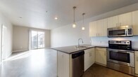 Located at 3490 Larimer St in Denver's vibrant River North Art District (RiNo), this contemporary single-floor unit showcases a clean, modern design with polished concrete floors throughout. The open-concept layout connects the kitchen and living area seamlessly, creating a generous and airy feel. The kitchen is well-appointed with light wood cabinetry, dark countertops, a peninsula island with a double-basin sink, and a full suite of stainless steel appliances including a refrigerator, range, microwave, and dishwasher. Pendant lighting above the island adds a warm, stylish touch. The living area is bright and open, benefiting from a sliding glass door that leads to a private balcony with views of the surrounding neighborhood. The bedroom is spacious and sun-filled, featuring large windows that invite abundant natural light and neighborhood views. The bathroom offers a wide vanity with dark countertops, light wood cabinetry, a large mirror, and a full tub-shower combination. A dedicated utility area includes an in-unit washer and dryer along with a water heater, plus additional closet and storage space. The unit's consistent use of neutral tones and concrete finishes creates a cohesive, urban-modern aesthetic throughout.