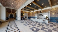 Located at Hardy Yards in Houston's 77009 corridor, this single-level amenity space draws on the area's rich railroad heritage to create a distinctive and memorable interior environment. The design's most striking feature is a long corridor with a barrel-vaulted exposed brick ceiling, where a floor inlay mimicking railroad tracks leads the eye toward a dramatic locomotive mural at the far end — a direct nod to the property's industrial history. Large-scale artwork lines the walls alongside seating areas furnished with classic wingback chairs, creating an inviting gallery-like passage.

The open gathering area transitions seamlessly into a well-appointed communal kitchen, defined by custom shaker-style cabinetry in soft grey, granite countertops, a tile backsplash, and stainless steel appliances including a commercial-grade refrigerator. Pendant bell lights hang above a kitchen island with bar seating. The checkered tile flooring anchors the space visually, extending throughout. Cozy banquette nooks feature tufted upholstered seating set against exposed brick walls with wall sconces and living vertical plant panels. Floor-to-ceiling glass walls open the space to a generous outdoor terrace with expansive city views, blending the interior's industrial-chic aesthetic with natural light and fresh air.