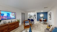 This single-floor residence showcases a thoughtfully designed open-concept layout that seamlessly connects the living, dining, and kitchen areas. Light wood-look flooring runs throughout, complementing crisp white walls accented by bold navy and slate-blue feature walls that add depth and character to the space.

The living area is bright and welcoming, benefiting from a sliding glass door that invites natural light and provides outdoor access. It flows naturally into a dedicated dining nook framed by a striking blue accent wall with a decorative round mirror. The galley-style kitchen is well-appointed with gray shaker cabinetry, granite countertops, a mosaic tile backsplash, and stainless steel appliances. A peninsula with bar seating bridges the kitchen to the open living space, enhancing both function and social interaction.

The primary bedroom features a soft blue accent wall, a walk-in closet, and ample space for a full furniture suite. A second bedroom offers natural light through a window with exterior views. The bathroom includes a granite-topped vanity with an undermount sink and a large mirror. Crown molding adds a refined touch throughout the common areas, contributing to the overall polished and contemporary ambiance of the residence.
