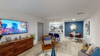 This single-floor residence showcases a thoughtfully designed open-concept layout that seamlessly connects the living, dining, and kitchen areas. Light wood-look flooring runs throughout, complementing crisp white walls accented by bold navy and slate-blue feature walls that add depth and character to the space.

The living area is bright and welcoming, benefiting from a sliding glass door that invites natural light and provides outdoor access. It flows naturally into a dedicated dining nook framed by a striking blue accent wall with a decorative round mirror. The galley-style kitchen is well-appointed with gray shaker cabinetry, granite countertops, a mosaic tile backsplash, and stainless steel appliances. A peninsula with bar seating bridges the kitchen to the open living space, enhancing both function and social interaction.

The primary bedroom features a soft blue accent wall, a walk-in closet, and ample space for a full furniture suite. A second bedroom offers natural light through a window with exterior views. The bathroom includes a granite-topped vanity with an undermount sink and a large mirror. Crown molding adds a refined touch throughout the common areas, contributing to the overall polished and contemporary ambiance of the residence.