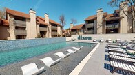 Located at 2501 Via Romana in Fort Worth, TX, Dixon is a thoughtfully designed residential community offering an exceptional array of amenity spaces. The centerpiece of the outdoor area is a stunning resort-style pool, complete with in-water lounge chairs and an expansive sundecked surrounded by ample seating. The pool area is framed by the community's multi-story Mediterranean-inspired buildings, featuring terracotta rooflines, private balconies, and decorative chimneys.

Inside the single-story clubhouse, residents are welcomed by a stylish lounge area furnished with leather sofas, accent chairs, and a large-screen TV, all set on dark-toned tile flooring. Glass partition walls open to a billiards room highlighted by an elegant chandelier, a full-sized pool table, and an area rug that adds warmth to the space. Natural light filters in through large windows, creating a bright and inviting atmosphere throughout.

A dedicated co-working area features solid wood communal tables, blue upholstered chairs, and sophisticated wall paneling with warm sconce lighting — ideal for focused work or collaboration. The corridors connecting the amenity spaces are adorned with vibrant artwork and exposed brick accent walls, adding an artistic character to the interior. A fitness center with modern cardio equipment rounds out the offerings, making Dixon a well-appointed community for comfortable living.