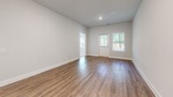 Located at 11911 Apache Ave in Savannah, Georgia, this single-story home offers a thoughtfully designed layout with a neutral color palette and a blend of wood-look flooring and plush carpet throughout. The open living and dining area is bathed in natural light from large windows and a front entry door with sidelights, showcasing smooth hardwood-style flooring and recessed lighting overhead. The space flows naturally into the kitchen, which features rich dark wood cabinetry, granite countertops, a tile backsplash, and black appliances including a range, microwave, and refrigerator. A kitchen island with pendant lighting provides additional workspace and visual separation from the living area. The bedrooms offer a comfortable, quiet atmosphere with soft carpeted floors and windows framing views of surrounding greenery. Two bathrooms serve the home; one includes a shower-tub combination with a white vanity, while the other features a walk-in shower and matching white cabinetry, both finished with wood-look flooring. A dedicated laundry room accommodates a full-size washer and dryer with overhead shelving for added storage convenience.
