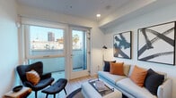 Located at 12023 Wilshire Blvd in Los Angeles, this single-floor unit offers a thoughtfully designed layout that balances comfort and contemporary style. The living area serves as the centerpiece of the space, featuring light wood flooring, recessed lighting, and crisp white walls that create a bright, airy atmosphere. Large glass doors open onto an outdoor balcony, flooding the room with natural light and framing views of the surrounding West Los Angeles cityscape, including palm trees and nearby high-rises. Bold abstract artwork adorns the walls, contributing to the modern aesthetic.

The kitchen is efficiently arranged in a U-shaped configuration, featuring wood-grain cabinetry with sleek hardware, white countertops, and a full suite of stainless steel appliances, including a gas range, microwave, dishwasher, and refrigerator. Recessed lighting illuminates the workspace effectively.

The bedroom is a calm retreat with clean white walls, light wood flooring, and a tall upholstered headboard as a focal point. A narrow window allows natural light to filter in while maintaining privacy.

The bathroom is finished in a clean, minimalist style with white subway tile surrounding a full soaking tub and shower combination, complemented by light tile flooring and bright white walls.