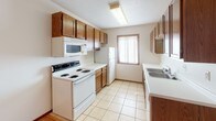 Located at 1415 34th St S in Fargo, North Dakota, this single-floor unit offers a practical and well-organized layout designed for comfortable everyday living. The kitchen is efficiently arranged with warm oak cabinetry lining both walls, white appliances including a coil-top range, built-in microwave, and refrigerator, light tile flooring, and a window that brings in natural light. The living area features light hardwood-style flooring near the entryway, transitioning to plush carpeting throughout the main living and sleeping spaces. A sliding glass door with vertical blinds provides access to the outdoors and allows additional natural light to fill the space. The bedrooms are generously proportioned, each with soft carpet, baseboard heating, and windows dressed with vertical blinds. One room also includes a wall-mounted air conditioning unit, ensuring year-round climate control. The full bathroom is finished with light tile flooring, a wood-toned vanity with mirror, and a tub-shower combination. Textured ceilings are consistent throughout the unit. The overall layout, as seen in the dollhouse view, is compact yet functional, with a clear separation between the kitchen, living, and sleeping areas.