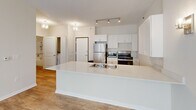 Located at 808 Berry St in Saint Paul, MN, this one-bedroom, one-bathroom unit offers a well-designed, single-floor layout that maximizes functionality and comfort. The open-concept living and kitchen area serves as the heart of the unit, where a generous white kitchen island with a double-basin sink anchors the space. White shaker-style cabinetry lines the kitchen walls, complemented by stainless steel appliances including a refrigerator, gas range, and microwave. Track lighting overhead adds a modern touch. Light hardwood-style flooring flows seamlessly throughout the main living areas, reflecting natural light that pours in through large windows dressed with vertical blinds. Wall sconces provide warm ambient lighting in the living room, which offers a bright, airy feel. The bedroom is a comfortable, well-proportioned retreat featuring a ceiling fan, a window for natural light, and a dedicated closet with built-in shelving for organized storage. The bathroom is thoughtfully designed with accessibility in mind, featuring sturdy grab bars and wood-look flooring. An in-unit laundry area is also visible, adding everyday convenience. The overall aesthetic is clean, neutral, and move-in ready.