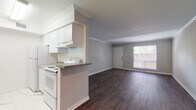 This single-story, 2-bedroom, 2-bathroom residence offers a thoughtfully arranged floor plan that balances communal and private living spaces. The living area greets residents with dark hardwood-style flooring, crown molding, and a ceiling fan, creating a clean and inviting atmosphere. A large window at the front of the living space allows natural light to fill the room, offering views of the greenery outside.

The kitchen is designed for efficiency, featuring white cabinetry with crown molding detail, granite-look countertops, white appliances including a range and refrigerator, and marble-look tile flooring. A peninsula counter with bar-height seating potential opens the kitchen toward the living area, promoting a connected, open feel.

Both bedrooms are carpeted for comfort and equipped with ceiling fans and windows that invite natural light. One bedroom features built-in shelving and dual closets, adding practical storage options.

The two bathrooms are finished with marble-look floor and wall tile throughout, extending up the full surround of each soaking tub. Granite-look vanity countertops and chrome or brushed-gold fixtures complete the polished, cohesive aesthetic. Overall, the unit presents a clean, updated interior with consistent finishes throughout.