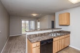 This single-floor unit offers a practical and well-organized layout that balances functionality with comfortable living. The kitchen serves as a central feature, equipped with light maple cabinetry, dark granite-style countertops, and a full suite of black appliances including an electric range, refrigerator, and dishwasher. Tile flooring runs throughout the kitchen and dining area, while a peninsula counter connects the kitchen to the carpeted living space, which benefits from natural light through a sliding glass door leading to an outdoor area.

The bedrooms are carpeted and finished in neutral tones, each featuring ceiling fans with integrated lighting. Windows in the bedrooms provide outdoor views of surrounding greenery and trees, lending a calm, natural atmosphere. Closet space is included in the bedrooms, with at least one room featuring a reach-in closet.

The bathroom is finished with tile flooring, a maple vanity with a dark countertop and a large mirror, and a walk-in shower stall with built-in shelving. Grab bars are installed near the shower and toilet, adding accessibility. Throughout the unit, neutral wall tones and consistent finishes create a cohesive and understated aesthetic.