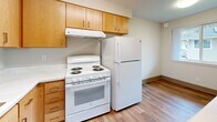 Located at 8415 NE Hazel Dell Ave in Vancouver, WA, this one-bedroom, one-bathroom unit offers a practical and comfortable layout across a single floor. The combined living, dining, and kitchen area forms the heart of the unit, with natural light streaming in through multiple windows. Light-toned carpet covers the living space, while durable wood-style flooring runs through the kitchen and entry areas.

The kitchen is efficiently designed with warm wood cabinetry providing generous upper and lower storage, a white electric range with overhead ventilation, a full-size refrigerator, and a sink with a wall-mounted fold-down counter that serves as a convenient dining or prep surface.

The bedroom is a comfortable, carpeted retreat featuring a sliding-door closet and a window with an outdoor view of the surrounding neighborhood, allowing for natural light. An additional closet elsewhere in the unit adds valuable storage capacity.

The bathroom is clean and straightforward, featuring a full tub-shower combination with built-in shelving, a toilet, and a wood-toned vanity with an integrated sink. Neutral wall tones and consistent finishes throughout the unit contribute to a cohesive and understated aesthetic. This unit is a functional and well-appointed space suited for single occupancy or couples seeking efficiency and simplicity.