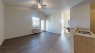 This single-floor residence showcases a thoughtfully designed open layout with notable architectural interest provided by vaulted ceilings throughout the main living areas and bedrooms. The living room is generously sized, featuring wood-look hard-surface flooring, a ceiling fan, and a wall-unit HVAC system. A sliding glass door and adjacent window allow natural light to fill the space. The kitchen connects seamlessly to the living area via a peninsula with bar seating. It is equipped with light wood cabinetry extending to the ceiling for ample storage, granite-style countertops, and black appliances including a range, over-the-range microwave, and refrigerator. The bedrooms are carpeted and well-lit, each featuring vaulted ceilings and multiple windows with blinds that offer views of the surrounding neighborhood. The bathroom is finished with matching light wood cabinetry, granite-style countertops, a large mirror, tile flooring, and a full tub-shower combination. Throughout the unit, neutral tones and clean white walls create a bright, cohesive aesthetic well-suited to a variety of interior styles.