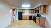 This single-floor unit offers a practical and well-organized layout centered around a fully equipped kitchen. The kitchen features warm honey-toned oak cabinetry providing generous upper and lower storage, complemented by granite-look countertops. Black appliances, including a full-size refrigerator, dishwasher, gas range with overhead microwave, and a double-basin sink, outfit the space with everything needed for everyday cooking. The flooring throughout the kitchen area is light-toned wood-look laminate, adding warmth and easy maintenance underfoot. Overhead fluorescent lighting ensures the kitchen remains bright and functional. A textured ceiling adds a subtle design detail throughout the space. Notably, a dedicated laundry area is accessible just off the kitchen through a doorway, housing a full-size washer and dryer — a convenient in-unit feature. The open flow between the kitchen and adjacent living areas allows for an easy, connected layout. Neutral wall tones and consistent flooring materials throughout contribute to a cohesive, understated aesthetic well-suited for comfortable day-to-day living.