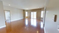 This well-appointed single-story home offers three bedrooms and two bathrooms across a generously sized floor plan. The living area immediately impresses with its rich, polished hardwood flooring that reflects natural light throughout the space, creating a warm and inviting ambiance. Neutral-toned walls provide a versatile backdrop, complementing the clean white baseboards and trim that frame each room. Recessed lighting in the ceiling adds a modern touch while ensuring the interior remains bright and well-lit at any time of day. A large sliding glass door serves as a focal point in the main living area, opening to an outdoor deck and flooding the space with an abundance of natural light. Flanking the sliding door are additional windows that further enhance the airy, open feel of the room. The thoughtful layout of this single-floor residence ensures easy accessibility and a seamless flow between living spaces. Ceiling-mounted HVAC vents are strategically placed to maintain year-round comfort throughout the home. The combination of practical design elements and quality finishes makes this a functional and attractive living space suited for a variety of lifestyles.