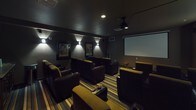 Located at 2865 W Elliot Dr in Spokane, WA, this dedicated single-floor private home theater is designed to replicate the immersive experience of a commercial cinema. The room is arranged with multiple rows of plush, dark leather and olive-upholstered reclining seats with built-in cup holders, positioned in a tiered layout to ensure clear sightlines to the screen from every seat. A large retractable projection screen dominates the front wall, paired with a ceiling-mounted projector for a true cinematic presentation. The space is finished with dark, moody wall tones that enhance contrast and minimize light reflection during screenings. Ambient wall sconces are strategically placed throughout, providing soft, directional lighting that evokes the atmosphere of a classic movie house. The floors are covered in a bold, multi-toned striped carpet that adds a theatrical design element. Classic framed movie posters line the side walls, reinforcing the cinematic theme. At the rear of the room, a concession-style counter area with a popcorn machine and additional storage adds a fun, authentic touch. A pair of bold red entry doors complete the theater aesthetic, making this space a fully immersive and thoughtfully designed entertainment destination.
