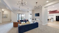 Located at 501 4th Ave SE in Cedar Rapids, Iowa, this thoughtfully designed single-floor amenity space offers a generous and versatile layout ideal for gathering, entertaining, and relaxing. The open-concept living room anchors the space with bold navy blue channel-tufted sofas, a cognac leather accent chair, and a striking floor-to-ceiling tile-clad fireplace wall with a mounted flat-screen TV. Sculptural sputnik chandeliers hang overhead, casting warm light across the carpeted lounge area, which opens through glass doors to an outdoor terrace. The fully equipped kitchen features white shaker cabinetry, subway tile backsplash, bold deep-red accent walls, and a large white waterfall island with bar seating — ideal for communal meals or catered events. Adjacent to the kitchen, a casual dining area with round tables and modern pendant lighting offers a relaxed setting with views to the exterior courtyard. A dedicated game room with light hardwood-style flooring provides space for a foosball table and additional recreation. Intimate private nooks, accented with rich burgundy ceilings and patterned wallpaper, offer quiet seating for two. Throughout, a curated palette of teal, burgundy, and white with contemporary artwork creates a vibrant yet welcoming atmosphere.