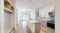 Located at 4040 Valley View Ln in Farmers Branch, TX, this thoughtfully designed 2-bedroom, 2-bathroom single-floor residence offers a clean, modern aesthetic throughout. The open-concept kitchen and living area serves as the heart of the home, anchored by a long quartz-topped island with an undermount sink and stylish pendant lighting. The kitchen is outfitted with two-tone cabinetry — white uppers paired with wood-grain lowers — a subway tile backsplash, and stainless steel appliances including a French door refrigerator and range. Light hardwood flooring flows throughout the main living areas, enhancing the bright, airy atmosphere. A built-in mudroom nook near the entry provides convenient shelving, hooks, and bench seating. The primary bedroom features its own en-suite bathroom complete with a dual-sink vanity, glass-enclosed shower, soaking tub, and wood-tone cabinetry. A spacious walk-in closet with corner shelving and dual hanging rods serves the primary suite. The second bedroom is carpeted and benefits from natural light through a window with blinds. The second bathroom mirrors the modern finishes seen throughout, with a single-sink vanity and tub-shower combo. A dedicated laundry room completes this well-appointed home.