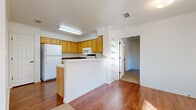 This single-story residence offers a well-organized layout featuring three bedrooms, three bathrooms, a living room, kitchen, hallway, and dedicated laundry room. The interior is finished with warm wood-look flooring throughout the main living areas and hallway, while the bedrooms feature plush carpeting for added comfort. Crown molding adds a clean architectural detail throughout.

The kitchen is equipped with warm honey-toned cabinetry, a peninsula with a breakfast bar overhang, dark tile backsplash, and white appliances including a refrigerator, electric range, and microwave. A built-in corner shelving unit adds a unique decorative touch near the kitchen entrance.

The living room is bright and open, with natural light streaming through multiple windows, complemented by a ceiling fan with light fixture. The bedrooms are similarly well-lit, each featuring ceiling fans and windows that bring in natural light. The primary bedroom offers a modest yet functional footprint.

Each of the three bathrooms features light wood cabinetry, white countertops, a single-sink vanity with mirror, and wood-look flooring. The full bathrooms include a shower-tub combination with grab bars. The laundry room includes upper cabinetry and a washer hookup, keeping daily chores neatly contained.