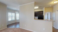 This single-story, 2-bedroom, 2-bathroom unit offers a thoughtfully designed layout that balances open communal spaces with private retreats. The living area is spacious and carpeted, featuring crown molding, a ceiling fan, and multiple windows that allow generous natural light to fill the room. A half-wall with a granite countertop visually connects the living space to the kitchen, creating an open-concept feel while maintaining distinct zones.

The kitchen is equipped with dark espresso cabinetry, black appliances including a refrigerator, stove, and dishwasher, and granite-style countertops. Wood-look flooring runs throughout the kitchen, adding warmth and durability. A door provides additional access and light to this functional cooking space.

Both bedrooms are carpeted and feature ceiling fans. One bedroom benefits from a window with exterior views, while the other offers a quieter, more enclosed setting. Each room provides comfortable proportions suitable for standard furnishings.

The two bathrooms are finished with wood-look flooring and dark vanity cabinetry. One bathroom includes a tub-shower combination with white tile surround, while the other features a well-lit vanity with a large mirror and chrome fixtures. Crown molding and consistent neutral tones throughout the unit create a cohesive, clean aesthetic.