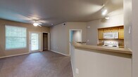 Located at 8603 N Loop 1604 W Access Rd in San Antonio, Texas, this single-floor unit offers a functional and comfortable layout with a cohesive neutral color palette throughout. The open living area is carpeted and bathed in natural light from large windows, with a ceiling fan overhead and a private exterior door leading to an outdoor space. A built-in closet provides convenient storage directly in the living area. The kitchen is positioned adjacent to the living space and features light wood cabinetry, a breakfast bar counter that opens to the main living area, a white electric range, an over-the-range microwave, and ample counter space — ideal for everyday meal preparation. Each bedroom is carpeted and equipped with a ceiling fan, offering tree-lined outdoor views through slatted blinds. The bedrooms provide a calm, comfortable retreat with clean walls and good natural light. The bathroom includes hardwood-style flooring, a light wood vanity with integrated sink and storage, a well-lit mirror, and a full tub and shower combo with white tile surround. Track lighting and recessed fixtures in key areas add supplemental illumination throughout the unit, completing this practical and well-appointed San Antonio residence.