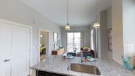 This 1-bedroom, 1-bathroom residence offers a thoughtfully designed open-concept layout that seamlessly connects the kitchen, dining, and living areas. The kitchen is a standout feature, boasting granite countertops with a speckled finish, a stainless steel undermount sink, and stylish pendant lighting that adds a modern touch overhead. The kitchen island serves as a natural gathering point, providing additional prep space and casual seating. The living area is bright and welcoming, benefiting from a large sliding glass door that opens to a private balcony, allowing ample natural light to fill the space and offering views of the surrounding community. Neutral gray walls and light flooring throughout create a clean, contemporary aesthetic. The bedroom, visible through an open doorway, features carpeted flooring and continues the light, neutral color palette. With its modern finishes, functional open floor plan, and access to outdoor space, this residence provides a comfortable and stylish living environment suited for everyday life.