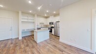 This single-story, 2-bedroom, 2-bathroom residence in Dallas, Texas offers a thoughtfully designed layout with modern finishes throughout. The open-concept kitchen serves as the heart of the home, featuring white shaker cabinets, granite countertops, a central island, stainless steel appliances including a refrigerator, range, and microwave, and durable wood-look flooring. A built-in desk area with open shelving adds a functional workspace within the kitchen. Recessed lighting illuminates the space, which flows seamlessly into the living area, where a door opens to an outdoor balcony framed by windows that bring in generous natural light. Both bedrooms are carpeted and fitted with ceiling fans and large windows overlooking lush tree canopy views, creating a calm and restful atmosphere. Each bedroom includes closet space, with the primary suite featuring a spacious en-suite bathroom equipped with a double-sink vanity topped with granite counters, wood-look flooring, and access to a walk-in closet. The second bathroom offers a full tub-shower combination with white tile surround and additional cabinet storage. A dedicated laundry area and ample closet space throughout complete this well-organized home.