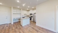 This single-story, 2-bedroom, 2-bathroom residence in Dallas, Texas offers a thoughtfully designed layout with modern finishes throughout. The open-concept kitchen serves as the heart of the home, featuring white shaker cabinets, granite countertops, a central island, stainless steel appliances including a refrigerator, range, and microwave, and durable wood-look flooring. A built-in desk area with open shelving adds a functional workspace within the kitchen. Recessed lighting illuminates the space, which flows seamlessly into the living area, where a door opens to an outdoor balcony framed by windows that bring in generous natural light. Both bedrooms are carpeted and fitted with ceiling fans and large windows overlooking lush tree canopy views, creating a calm and restful atmosphere. Each bedroom includes closet space, with the primary suite featuring a spacious en-suite bathroom equipped with a double-sink vanity topped with granite counters, wood-look flooring, and access to a walk-in closet. The second bathroom offers a full tub-shower combination with white tile surround and additional cabinet storage. A dedicated laundry area and ample closet space throughout complete this well-organized home.