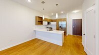 Located at 101 Woodbine Road in Downingtown, PA, this well-appointed one-bedroom, one-bathroom residence offers a thoughtfully designed single-floor layout with modern finishes throughout. The open-concept kitchen serves as a central highlight, featuring a sleek peninsula with a white quartz countertop, pendant lighting, and a full suite of stainless steel appliances including a gas range, built-in microwave, and a side-by-side refrigerator with water dispenser. Warm wood-toned upper cabinetry paired with crisp white lower cabinets adds a contemporary, two-tone aesthetic, while light hardwood-style flooring extends throughout the main living area. The generously sized bedroom offers plush carpeting, neutral-toned walls, and multiple windows that invite an abundance of natural light and outdoor views, creating a calm and restful retreat. A dedicated closet provides ample storage. The bathroom is finished in a clean, modern style with white subway tile surrounding the soaking tub and shower, a wood-vanity with an undermount sink, white countertop, and a large wall mirror. In-unit laundry hookups are also present. The overall ambiance is bright, clean, and contemporary, making this a practical and stylish residence in the heart of Downingtown.