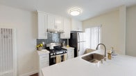 This single-floor residence is designed with a bright, clean aesthetic and a practical, well-organized layout. The open-concept living and kitchen area serves as the heart of the unit, where wood-look flooring extends seamlessly throughout, complementing the neutral, warm-toned walls. A large window dressed with vertical blinds floods the living space with natural light, while a wall-mounted climate control unit ensures year-round comfort.

The kitchen is a standout feature, showcasing white shaker cabinetry, light quartz countertops, and a contrasting slate-blue subway tile backsplash. Stainless steel appliances, including a gas range with hood and a refrigerator, are complemented by a peninsula with an undermount sink and brushed nickel faucet, offering additional prep space and a natural divide between the kitchen and living areas.

The bedrooms are generously proportioned, each featuring the same wood-look flooring, neutral walls, and vertical blind-covered windows that invite natural light. The unit includes two bathrooms: one with a tub-shower combination, wood-look flooring, and a white vanity, and a second with a separate shower, a wide white vanity with ample cabinet storage, and a large mirror. Both bathrooms carry the same clean, cohesive design found throughout the rest of the unit.