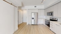 This thoughtfully designed 3-bedroom, 3-bathroom unit at 103 W Camino Real, #318 offers a clean, modern aesthetic throughout its efficiently laid-out single-floor plan. Light wood-style flooring flows seamlessly across every room, creating a cohesive and airy feel. The contemporary kitchen is well-appointed with floor-to-ceiling light wood cabinetry, stainless steel appliances including a side-by-side refrigerator, electric range, microwave, and dishwasher, complemented by track lighting and a neutral countertop with an undermount sink. Each bedroom features large windows with views of lush tropical greenery, ceiling fans for comfort, and bright white walls that maximize natural light. Two walk-in closets with wire shelving systems provide ample organized storage. The three bathrooms are finished to a high standard — one features a full-width glass-enclosed walk-in shower with large-format tile surround and a rainfall showerhead, while another includes a soaking tub and a wood-toned vanity with a generous mirror. An outdoor space with white stucco walls opens to sweeping views of palm trees and blue skies, adding a true Florida resort ambiance to this well-appointed residence.