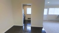 This single-floor residence offers a clean, functional layout with a cohesive and understated aesthetic throughout. The interior is finished with high-gloss dark ceramic tile flooring that reflects light beautifully, creating a sleek and polished look underfoot. Neutral, warm-toned walls provide a versatile backdrop that complements a variety of décor styles.

A dedicated laundry room is a standout practical feature of the space, accessible through a well-framed interior doorway. This utility area is equipped with a stacked washer and dryer unit alongside a refrigerator, making efficient use of the available space. A window in the laundry room allows natural light to filter in, keeping the area bright and well-ventilated. A floor-level heating vent ensures comfort in this functional zone.

The transition between rooms is marked by clean white door casings and baseboards that provide crisp contrast against the darker flooring. Adjacent areas suggest a carpeted zone, offering a textural shift that distinguishes living spaces from utility and tiled areas. The overall ambiance is tidy and move-in ready, with an emphasis on practicality and straightforward design. Natural light is present in multiple areas, contributing to an open and airy feel throughout the home.