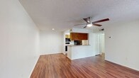 This 540 square foot apartment at Lakewood Place offers a well-designed living space with one bedroom and one bathroom. The open floor plan maximizes the use of space, seamlessly blending the kitchen, living, and dining areas. The kitchen features wooden cabinetry, a full-size refrigerator, and ample counter space with a sink and electric stove. 

The living area boasts warm-toned wood flooring and is illuminated by a modern ceiling fan with integrated lighting. A sliding glass door provides access to an outdoor patio, bringing in natural light and offering a connection to the outdoors. The bedroom, measuring 130 square feet, includes carpeting for comfort and a ceiling fan for air circulation. It also features a large window and a walk-in closet for storage.

The bathroom is equipped with a shower/tub combination and has white tiled walls for a clean, bright appearance. Throughout the apartment, neutral-colored walls create a blank canvas for personalization. The unit's efficient layout includes a hallway connecting the various spaces, ensuring easy navigation within the compact floor plan.