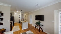 This thoughtfully designed 1-bedroom, 1-bathroom model unit in Humble, TX offers a well-appointed single-floor layout that balances comfort and functionality. The open-concept living and kitchen area is anchored by warm hardwood flooring and elegant crown molding throughout, giving the space a polished, cohesive feel. The living room features large windows dressed with layered blinds and drapes that flood the area with natural light while offering views of the surrounding greenery. A wall-mounted flat-screen television and glass-top accent table complete the space.

The kitchen is efficiently designed with dark cabinetry, granite countertops, stainless steel appliances including a refrigerator, electric range, and built-in microwave, as well as a double-basin sink set into a peninsula that opens toward the living area. Track lighting overhead provides ample illumination throughout the kitchen and connecting hallway.

The bedroom is a serene retreat featuring plush carpeting, a ceiling fan, and natural light filtering through curtained windows. It offers generous space for furniture and provides a calm, restful atmosphere.

The bathroom is clean and functional, featuring a soaking tub and shower combination with tile surround accents and classic fixtures. This model unit presents a well-rounded and welcoming living environment.