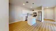 Located at 888 Delaware Ave in Buffalo, NY, this single-floor unit showcases a thoughtfully designed layout with modern finishes throughout. Light-toned luxury vinyl plank flooring runs continuously across the space, creating a cohesive and clean aesthetic from room to room.

The kitchen is a standout feature, outfitted with crisp white shaker-style cabinetry extending to the ceiling for ample storage, quartz-style countertops, and a full suite of stainless steel appliances including a refrigerator, electric range, microwave, and dishwasher. A central island with a matching quartz surface provides additional prep space and is accented by a stylish bronze pendant light overhead.

The open living area benefits from floor-to-ceiling windows that invite generous natural light and offer views of the surrounding Delaware Avenue neighborhood. Recessed lighting and neutral warm-gray walls contribute to the bright, airy atmosphere throughout.

The bedrooms are well-proportioned with large windows and clean, neutral finishes. The bathroom is outfitted with a glass-enclosed walk-in shower featuring white subway tile surround, a built-in niche, chrome fixtures, and a rainfall-style showerhead, delivering a polished, contemporary look.