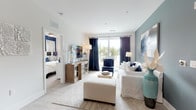 This thoughtfully designed single-floor residence showcases a cohesive coastal-inspired aesthetic, combining navy, slate blue, and crisp white tones throughout its open layout. The living room serves as the heart of the home, featuring light wood-style flooring, a sliding glass door opening to a private balcony with outdoor views, and a muted blue accent wall adorned with large-scale abstract artwork. White slipcovered seating, a woven area rug, and a wood media console create an inviting, relaxed atmosphere.

The kitchen is both functional and visually striking, with a two-toned cabinetry scheme pairing light gray upper cabinets with dark lower cabinets, white quartz countertops, a subway tile backsplash, and stainless steel appliances. A central island with seating provides an ideal casual dining spot. Adjacent to the kitchen, the formal dining area features a rustic wood table beneath an orb chandelier, with bold navy and gold artwork anchoring the space. An in-unit washer and dryer is conveniently tucked nearby.

The two bedrooms are distinctly styled: one features a bold navy accent wall with carpeted flooring and a ceiling fan, while the other showcases a softer slate blue palette with warm, earthy décor. The bathroom offers marble-look tile flooring, dark wood vanity cabinetry, and a full soaking tub.