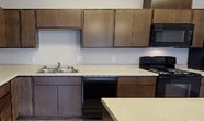 Located at 5805 S Ben Burr Rd in Spokane, Washington, this single-floor unit offers a clean, contemporary design with a cohesive aesthetic carried throughout every room. Wood-look vinyl plank flooring runs continuously across the living, kitchen, and bedroom areas, lending a warm yet modern feel to the space.

The open-concept kitchen is a functional centerpiece, featuring rich dark-toned cabinetry with ample upper and lower storage, light-colored countertops, and a full suite of black appliances including a refrigerator, electric range, built-in microwave, and dishwasher. A central kitchen island with pendant lighting provides additional prep space and serves as a natural divider between the kitchen and the expansive living area. The generous living area benefits from multiple windows and a sliding glass door that invite natural light and provide exterior views.

The bedrooms are well-proportioned, each featuring wood-look flooring, black-framed windows with exterior views, and baseboard heating. The bathroom is neatly appointed with wood-toned cabinetry, a full tub and shower combination, and consistent flooring that ties the space together. A dedicated entry corridor with a paneled white door provides a clear transition into the unit. Overall, the space presents a practical and well-designed layout suited to comfortable everyday living.