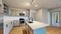 This single-floor residence offers a thoughtfully designed layout with contemporary finishes throughout. The kitchen is a standout feature, showcasing gray shaker-style cabinetry with matte black hardware, light granite countertops, and a herringbone-patterned tile backsplash. A central island with an undermount sink and matching granite surface provides additional prep space and casual seating. Stainless steel appliances, including a French door refrigerator, electric range, and built-in microwave, complete the kitchen. Light hardwood-style flooring runs throughout the main living areas, complementing the bright, neutral color palette. The open living area benefits from natural light through a large sliding glass door fitted with vertical blinds. Bedrooms are carpeted for comfort and feature natural light from double windows with blinds, along with ceiling fans. A generously sized walk-in closet with wire shelving and basket storage offers ample organization. The bathrooms are finished with granite-topped vanities, gray cabinetry, and wood-look flooring. One bathroom includes a soaking tub and shower combination with floor-to-ceiling white subway tile. Clean architectural details, such as five-panel interior doors and recessed lighting, contribute to the space's polished, modern aesthetic.
