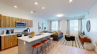 This thoughtfully designed 1-bedroom, 1-bathroom residence offers a seamless open-concept layout that maximizes functionality and flow. The combined kitchen and living area serves as the heart of the home, where light hardwood flooring, recessed lighting, and crisp white walls create a bright, contemporary atmosphere. The kitchen is equipped with stainless steel appliances, warm wood-grain cabinetry, a classic white subway tile backsplash, and a generous island with a white quartz countertop and bar seating — ideal for casual dining and entertaining. The adjoining living room receives abundant natural light through a bank of large windows dressed with sheer gray curtains, offering an open, airy feel.

The spacious primary bedroom is carpeted and flooded with natural light from multiple windows and a glass door that opens directly to a private balcony with outdoor views. The bedroom provides ample storage with multiple closets. The full bathroom features a wood-tone vanity with a white countertop, a large mirror, and a checkered tile floor, maintaining the cohesive modern aesthetic found throughout the residence. Clean lines, neutral tones, and quality finishes define this well-balanced and comfortable living space.