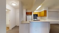This single-floor unit is thoughtfully laid out to maximize functionality and open living. The kitchen serves as a central feature, showcasing warm honey-toned wood cabinetry, a full suite of appliances including a white refrigerator, electric range, and built-in microwave, all illuminated by overhead fluorescent lighting. A curved peninsula counter extends into the living space, creating a natural division between the kitchen and the open living area while offering additional prep and seating space.

The living area is generously sized, finished with wall-to-wall neutral carpeting that continues throughout the unit, lending a cohesive and comfortable feel. A sliding glass door in the main room allows natural light to filter in and provides access to an outdoor area, enhancing the sense of openness.

A full bathroom is conveniently accessible from the main living space and features a clean, white soaking tub and shower combination with smooth wall surrounds and chrome fixtures, offering a simple and functional design. The overall color palette of the unit is bright and neutral, with white walls and light-toned trim throughout, creating an airy and welcoming ambiance. The floorplan, as seen from the overhead view, reflects a compact yet efficient use of space suited for comfortable everyday living.