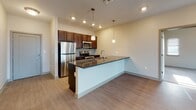 This single-floor unit offers a thoughtfully designed layout with a seamless blend of modern finishes and functional living spaces. The open-concept kitchen serves as the heart of the home, anchored by a large island with dark granite countertops and an integrated sink, pendant lighting overhead, rich dark-wood cabinetry, a herringbone tile backsplash, and a full suite of stainless steel appliances. The kitchen flows naturally into the main living area, which features smooth hardwood-style flooring, recessed lighting, and large windows fitted with blinds that invite natural light and frame elevated views of the surrounding cityscape. The bedrooms are carpeted for comfort, offering a calm retreat with generous wall space and windows overlooking the urban landscape. A standout feature of the primary bedroom is the expansive walk-in closet, outfitted with multi-tiered wire shelving systems and hanging rods along multiple walls, providing ample and organized storage. The bathroom is finished with light tile flooring, a granite-top vanity with dark wood cabinetry, a framed mirror, and a walk-in shower. Throughout the unit, neutral warm tones and consistent finishes create a cohesive, move-in-ready environment suited for modern urban living.