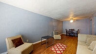 This single-floor residence offers a practical and cohesive layout across two bedrooms and two bathrooms. Throughout the common areas, warm wood-look flooring runs continuously, complementing the cool gray-toned textured walls that are consistent across every room. The living area provides an open, versatile space with natural light filtering through horizontal blinds, casting distinctive patterns across the walls. It flows directly into a dedicated dining area, which features a ceiling fan with integrated lighting overhead—a functional detail that adds both comfort and ambiance.

The galley-style kitchen is lined with white cabinetry on both sides, offering ample storage, along with light-speckled countertops and white appliances including a refrigerator and stovetop range. The efficient layout maximizes usability within the space.

Both bedrooms are carpeted and share the same gray textured wall finish and textured ceilings. The primary bedroom is generously sized with a window that allows natural light in, while the second bedroom similarly features a window. Each room offers comfortable proportions suitable for standard bedroom furniture.

The bathrooms include a white vanity with under-cabinet storage, a mirror, and a separate toilet and tub/shower area with tile surround, all finished with the same wood-look flooring found in the main living spaces.
