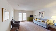 Located at 7612 Timberlake Rd in Lynchburg, Virginia, this single-floor residence offers a practical and comfortable layout across several well-appointed rooms. The living area is generously sized, featuring soft carpeting, neutral walls, and a pair of French doors that invite natural light and provide outdoor access. The space is versatile, accommodating both a seating arrangement and additional lounge chairs, making it ideal for relaxing or entertaining.

The kitchen is efficiently designed with warm honey-toned cabinetry, green countertops, and tile flooring. It is fully equipped with a white electric range, microwave, refrigerator, and dishwasher, along with ample upper and lower cabinet storage and a sink with a window view.

The residence includes two carpeted bedrooms, each offering a comfortable and quiet retreat. Both rooms feature windows that bring in natural light and provide adequate space for standard bedroom furnishings. The neutral color palette throughout lends a calm, cohesive feel.

Two full bathrooms serve the home, each featuring tile flooring, a vanity with under-sink storage, a large mirror, and a shower-tub combination. The consistent use of light tones and practical fixtures throughout the bathrooms maintains the home's clean, functional aesthetic.