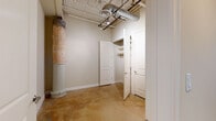 This two-bedroom, one-bathroom loft-style space spans two floors, offering a compelling blend of industrial heritage and contemporary design. The main level showcases an expansive open-plan living and kitchen area defined by polished concrete floors, exposed ductwork, coffered metal ceilings, and prominent structural columns that speak to the building's industrial origins. The kitchen is well-appointed with dark espresso cabinetry, granite countertops, stainless steel appliances, a central island with breakfast bar seating, and pendant lighting overhead. Large multi-pane windows framed by original exposed brick walls flood the space with natural light, adding warmth and texture to the interior. A sleek staircase with a rich wood railing and metal cable detailing connects the two floors, passing beneath striking exposed steel trusses that serve as a dramatic architectural focal point. The upper level houses the bedrooms, including a generously sized primary bedroom with a dedicated walk-in closet featuring built-in shelving. The bathroom is finished with granite countertops, dark wood cabinetry, a glass-enclosed tile shower, and polished tile flooring. Additional storage is provided by a well-organized hallway closet. Throughout the space, the interplay of raw industrial elements and refined modern finishes creates a distinctive and functional living environment.